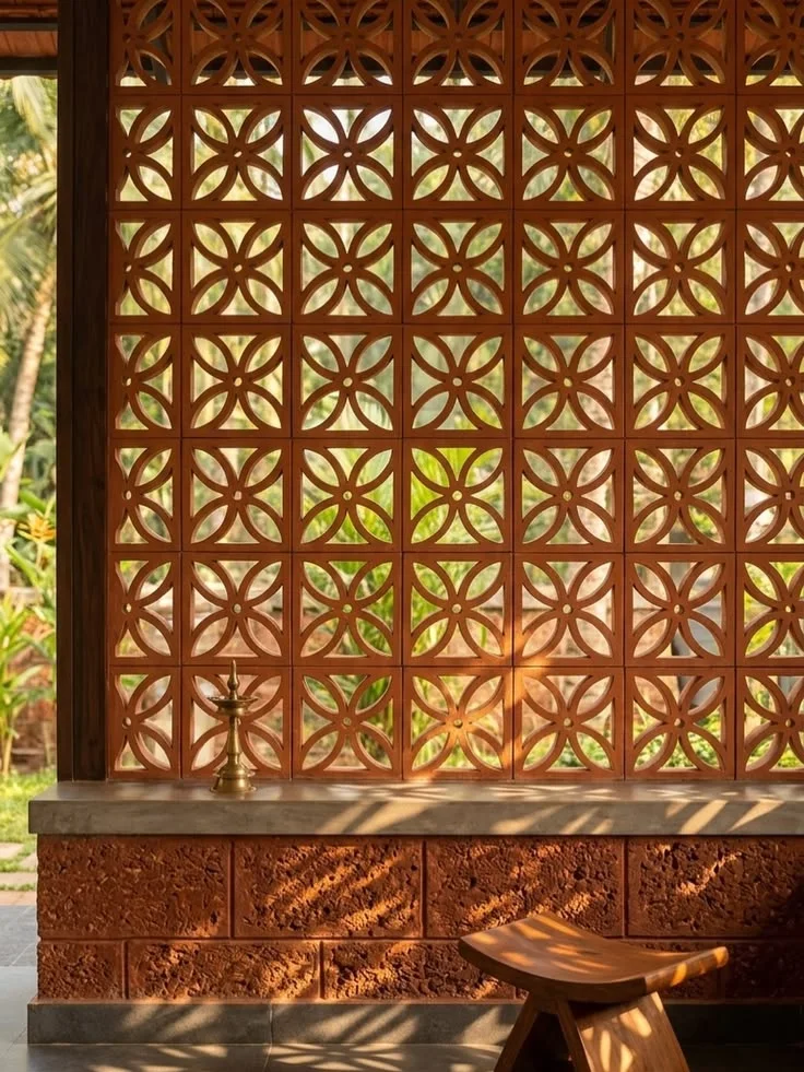 Terracotta jaali screen wall with warm sunlight and greenery visible through the perforations